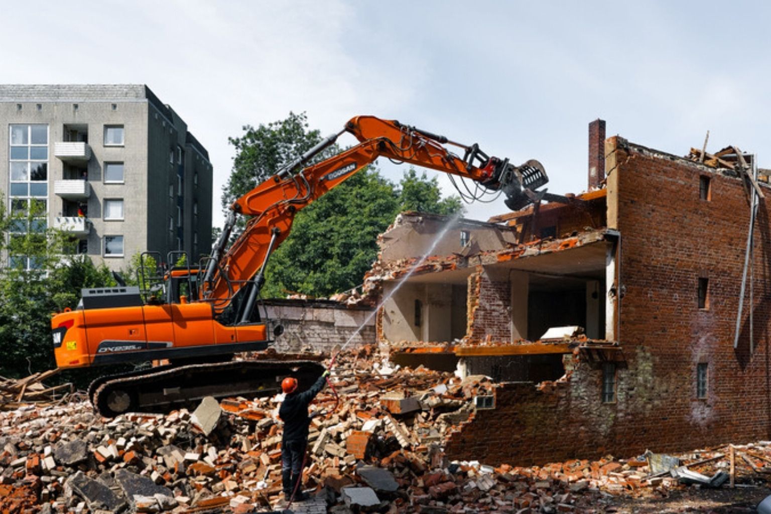 Orange gravemaskine river et murstenshus ned mellem boligblokke